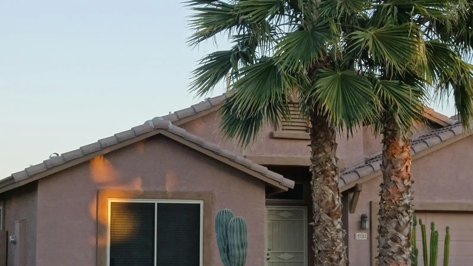 Stucco desert house under a clay tile roof, framed by palms in the evening light
