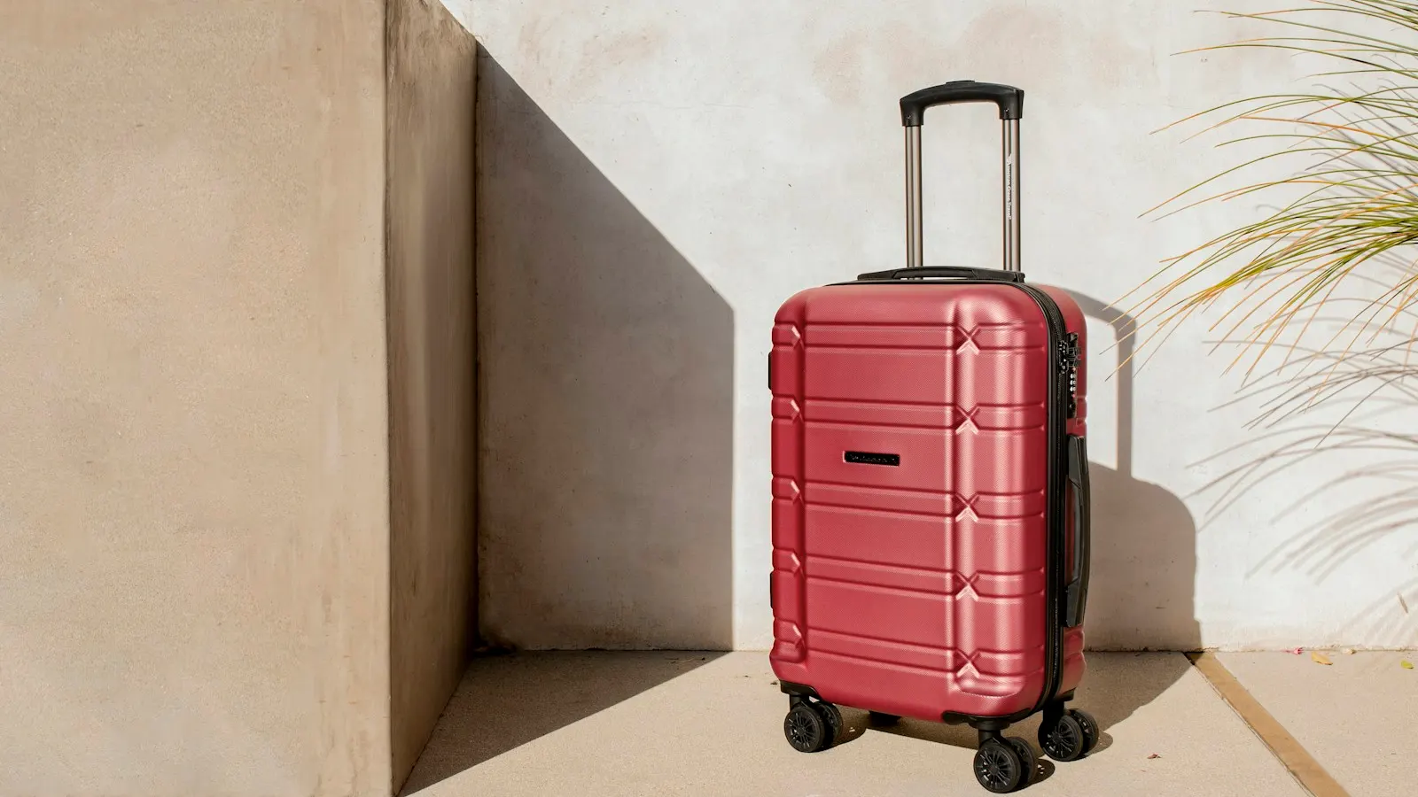 Packed red suitcase standing against a sunlit stucco wall