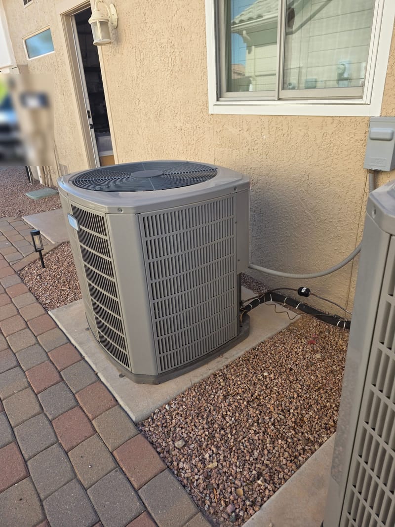 Outdoor air conditioning condenser on a concrete pad beside a stucco wall and a brick paver walkway