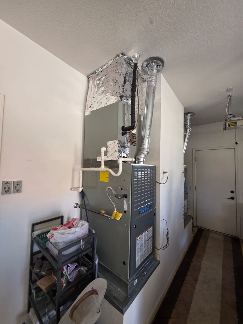 Gas furnace and air handler with foil wrapped duct work and a white condensate drain line on a garage wall