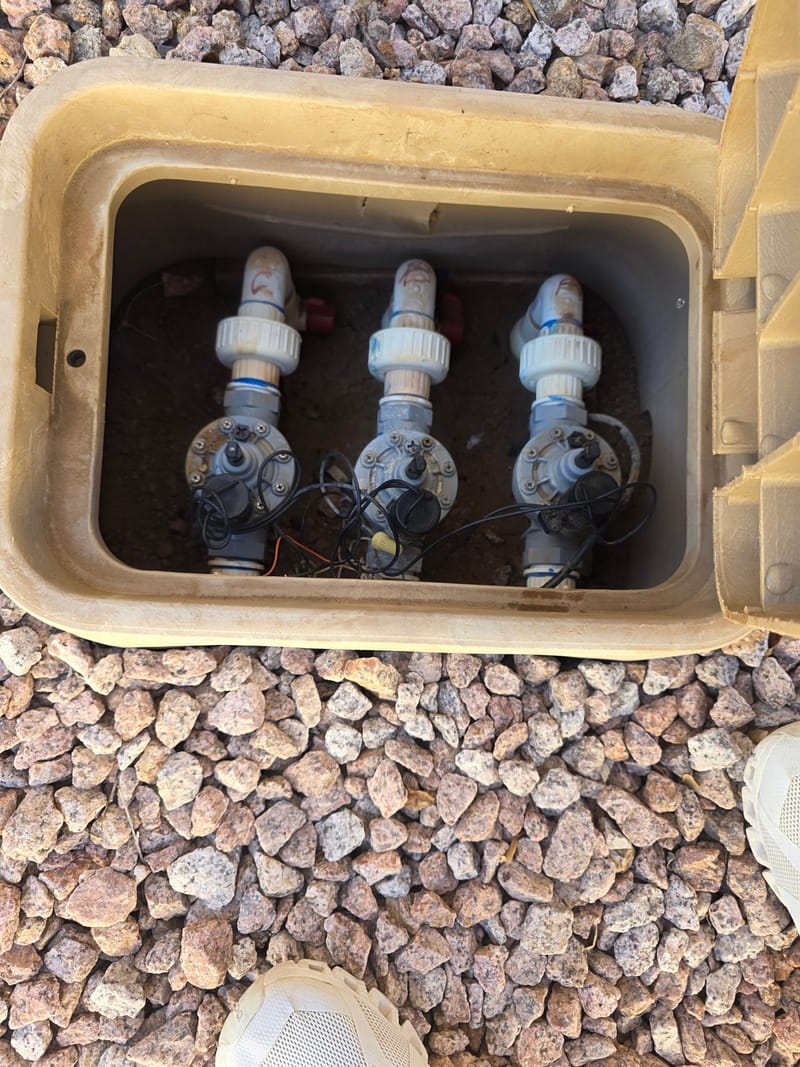 Open irrigation valve box holding three valves in gravel