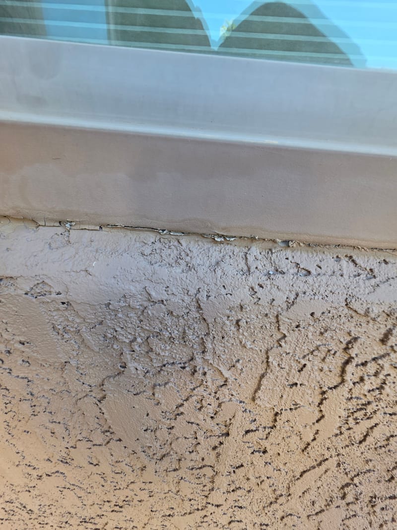Cracked and peeling sealant where a window sill meets a stucco wall